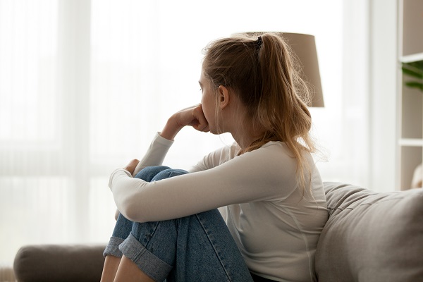 Young woman sat on sofa with knees raised looking out of the window
